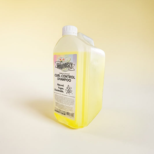Houndsly Curl Control Dog Shampoo in Vanilla & Sea Salt scent, a yellow liquid in a clear bottle with a white cap.